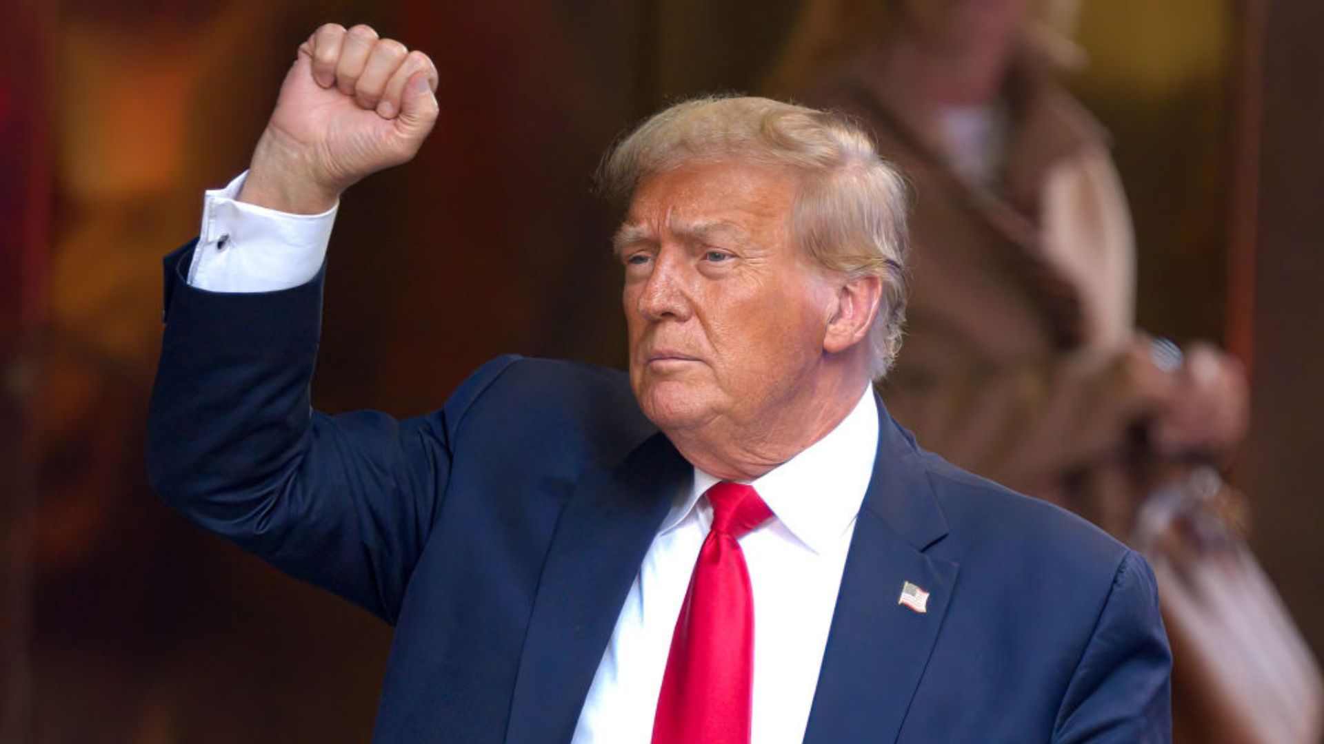 Donald Trump in a suit and red tie holding up his fist