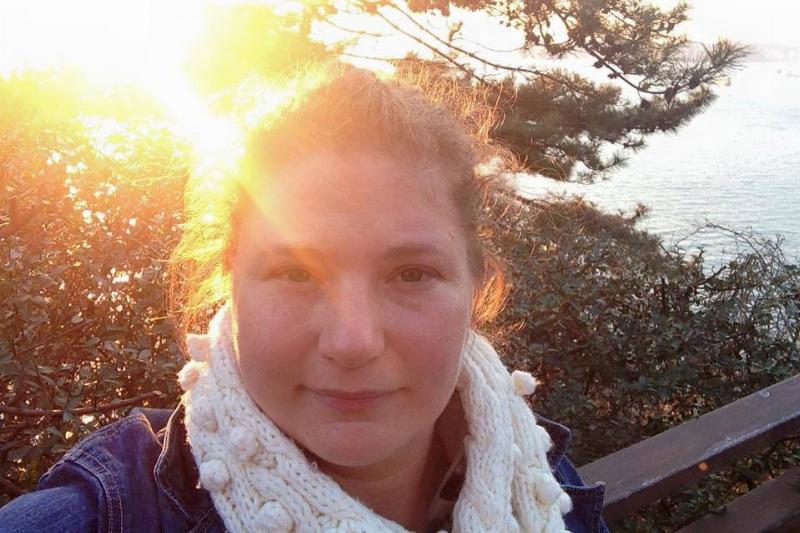 A woman takes a selfie during golden hour, with the sun casting a warm glow on her face