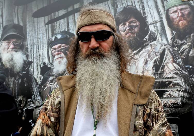 Phil Robertson stands in front of a backdrop featuring characters from the Duck Dynasty show