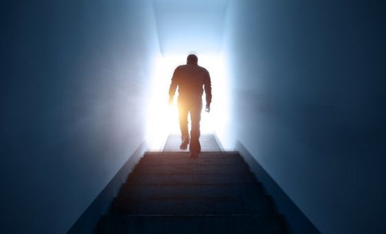 A silhouette of a man walking while facing a bright light source.