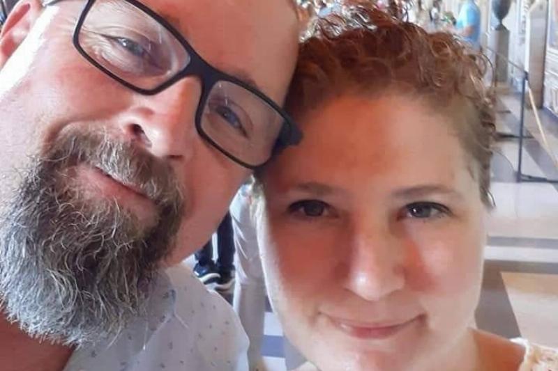 A close-up selfie of a couple; a bearded man with glasses on the left and a woman with curly hair on the right