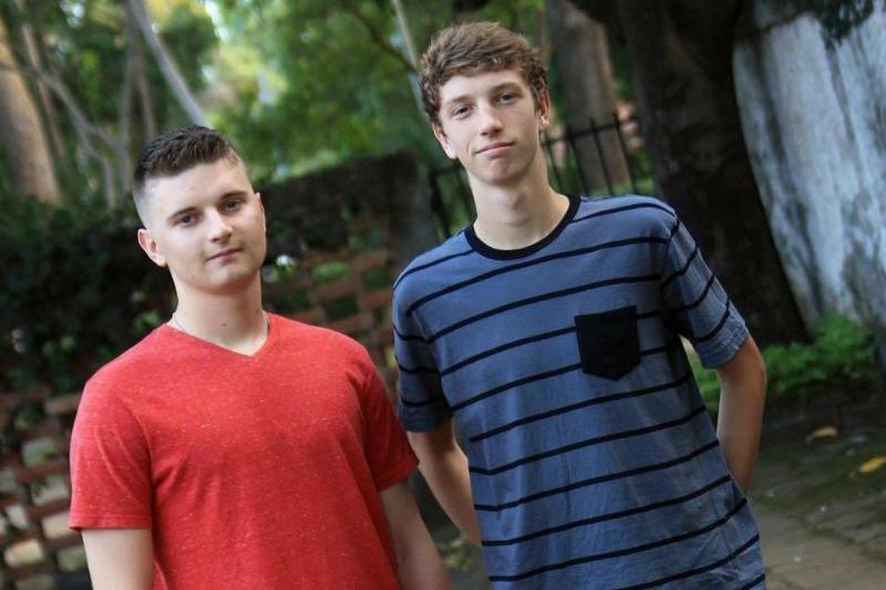 Two young men standing outdoors with a backdrop of greenery and stone steps