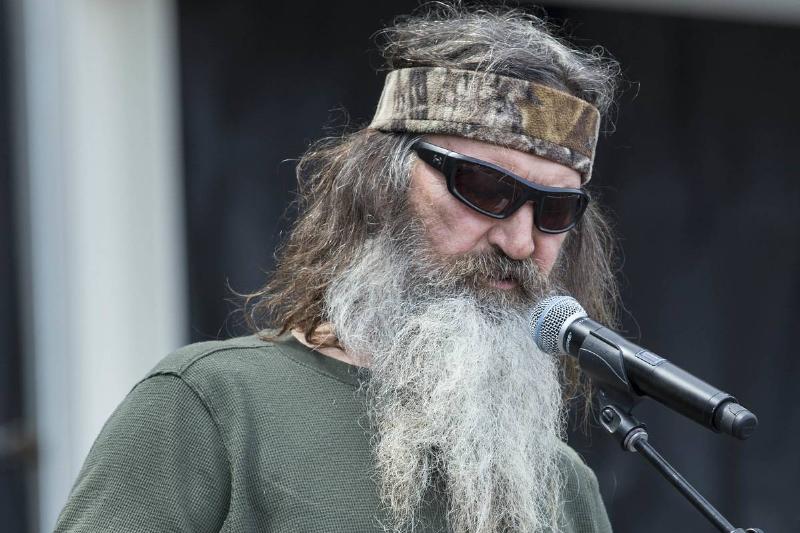 Phil Robertson wears a camo headband and stands next to a microphone