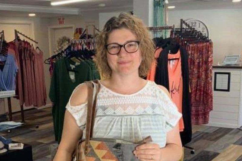 A woman with blond curly hair wearing glasses, smiles whilst in a store